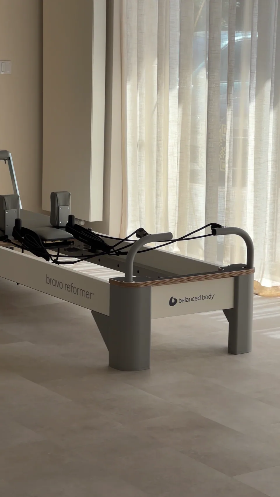 Reformer Balanced Body Bravo ustawiony przy dużym oknie z jasną zasłoną.